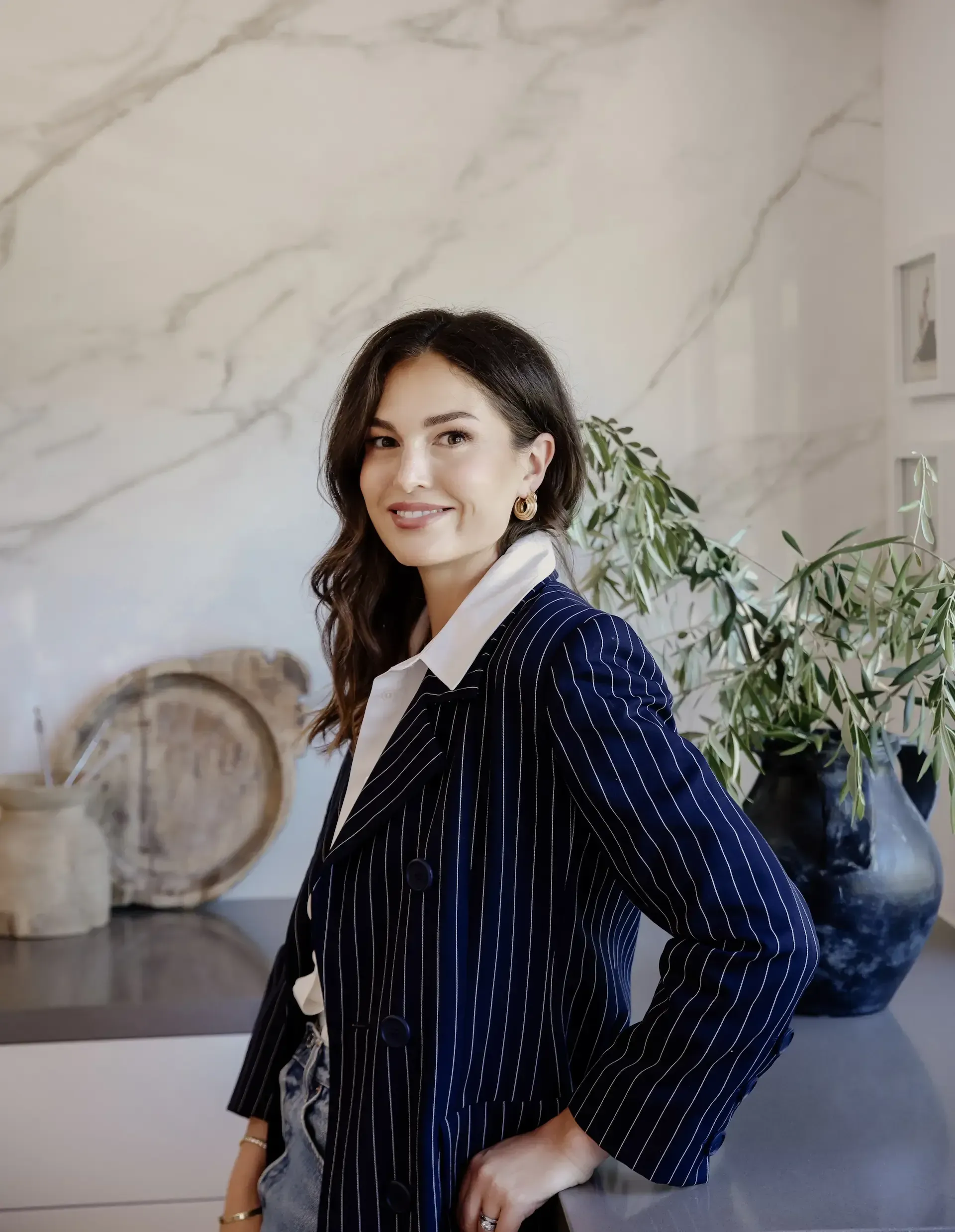 Professional interior designer in pinstripe blazer standing in elegant marble kitchen with plants and refined styling House Rupert interior design Santa Barbara and Montecito